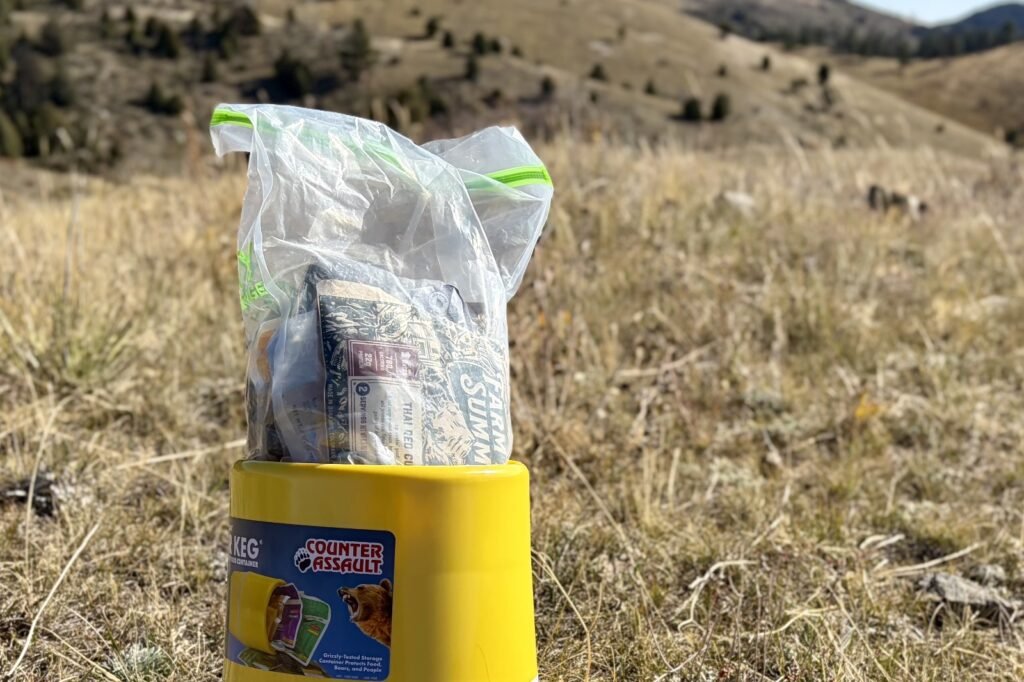 a clear bag full of food sticks out of the top of a yellow bear canister