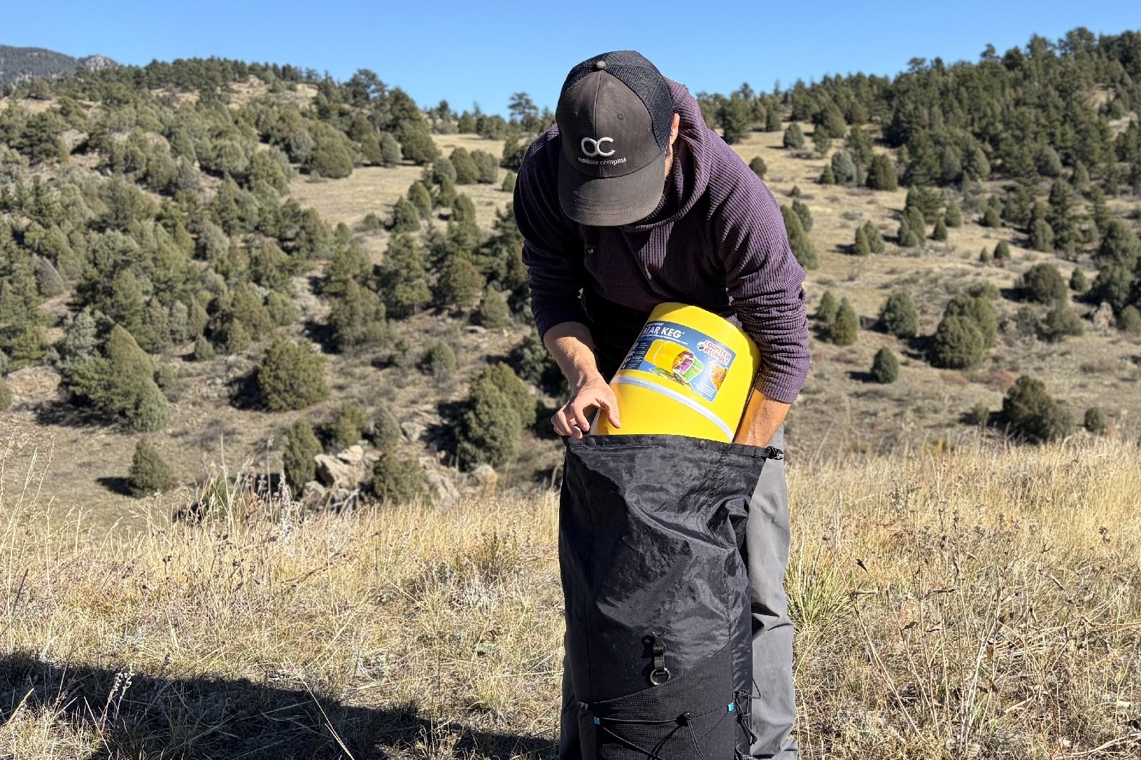 a hiker packs a yellow bear canister into a black backpack