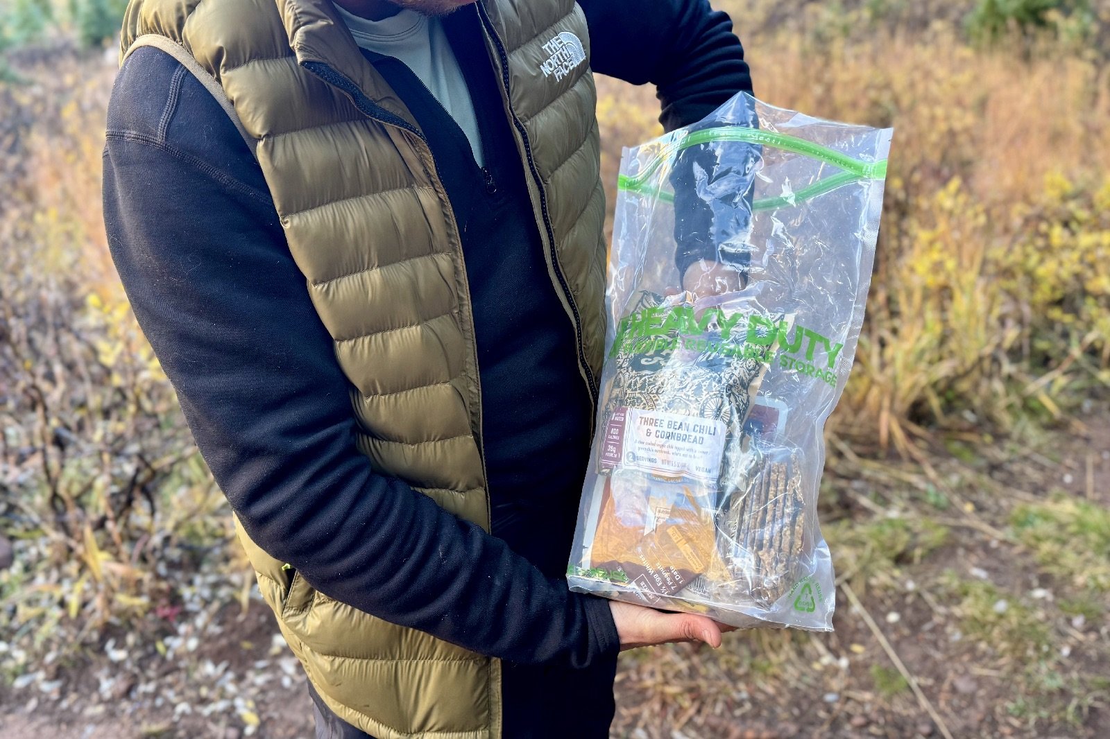 a hiker reaches his arm into a large clear plastic bag full of food.