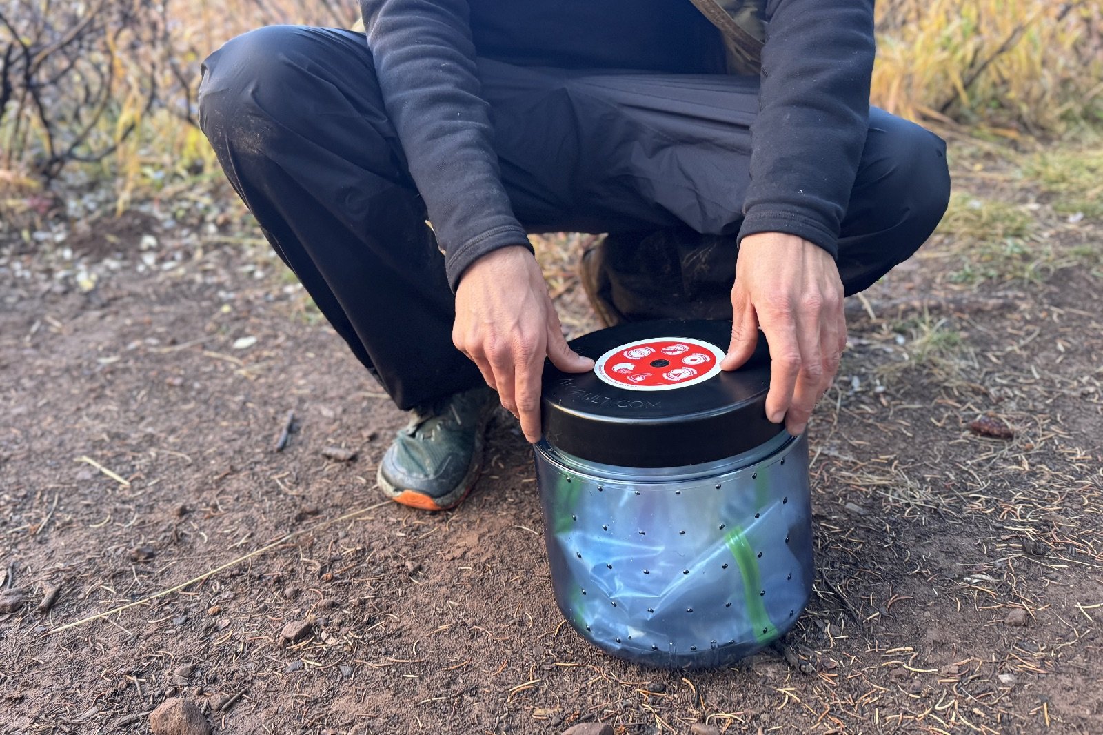 a hike squats down next to a blue bear canister