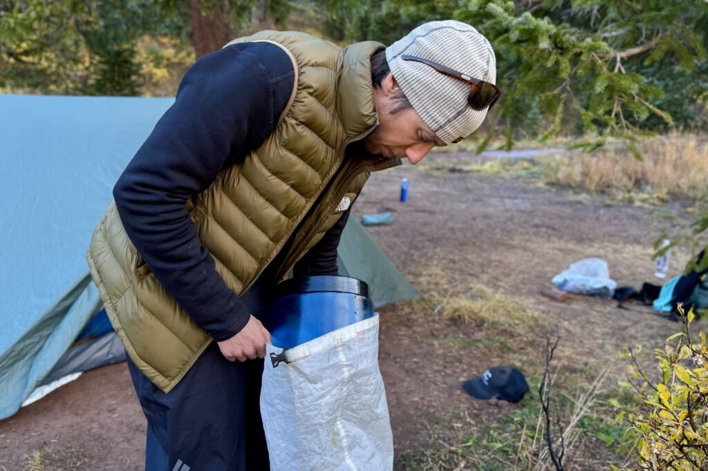 a hiker squeezes a blue bear canister into a backpack