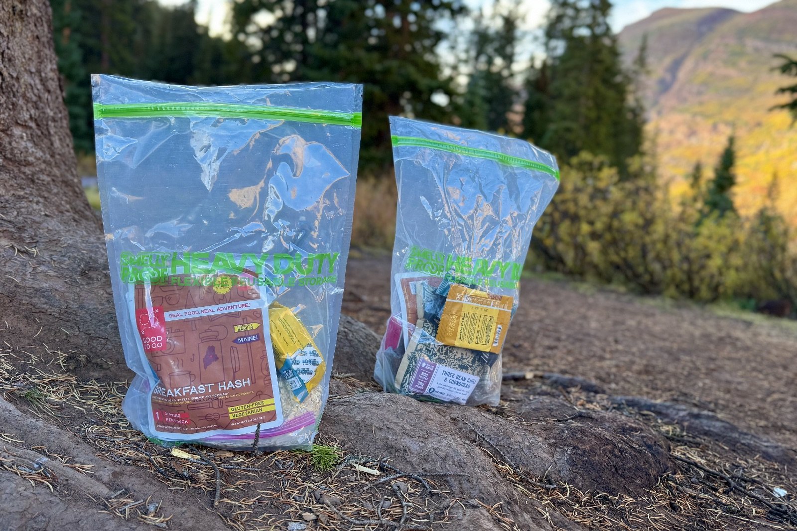two large plastic bags sit side by side on the ground filled with backpacker food
