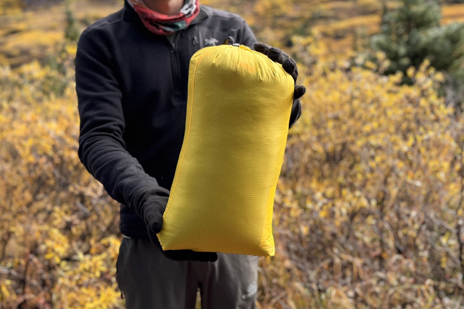 a hiker holds a sleeping bag in a yellow stuff sack