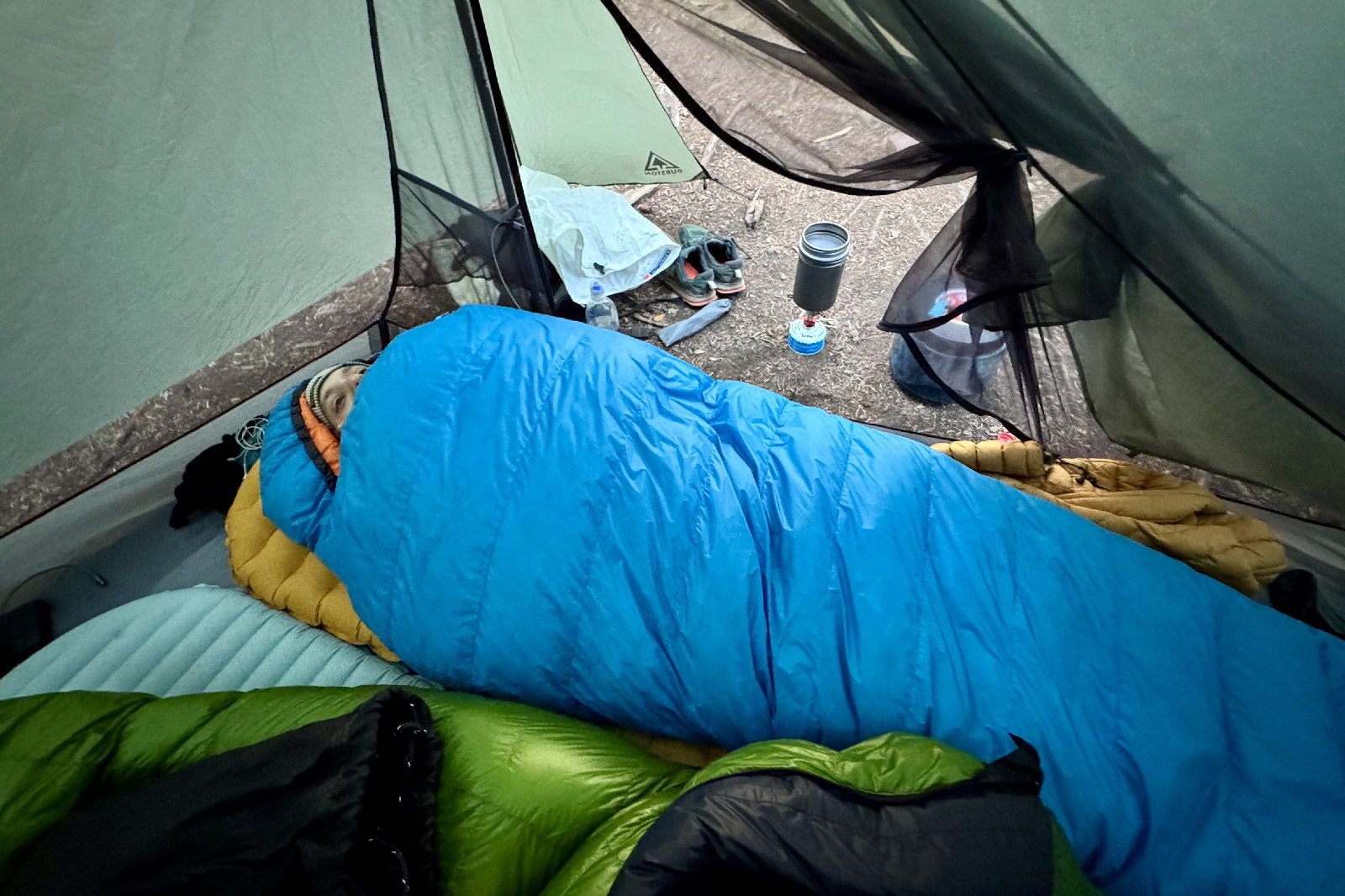 a hiker lays in a blue sleeping bag in a tent