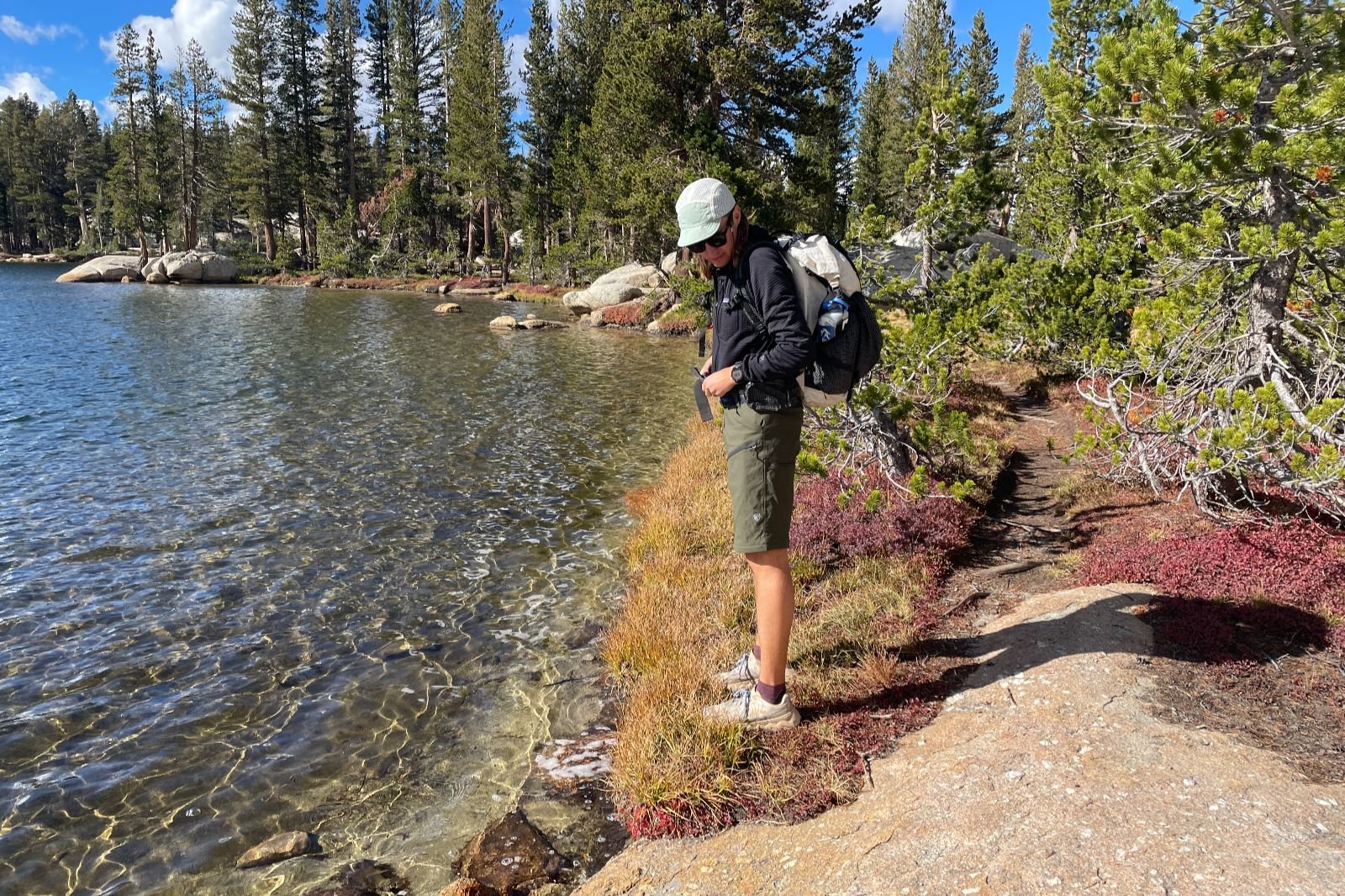 A man stands in green shorts along an alpine lake.