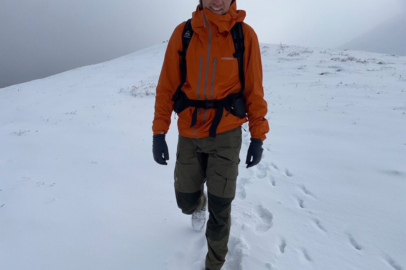 A man hikes through a snowy landscape wearing an orange rain jacket.