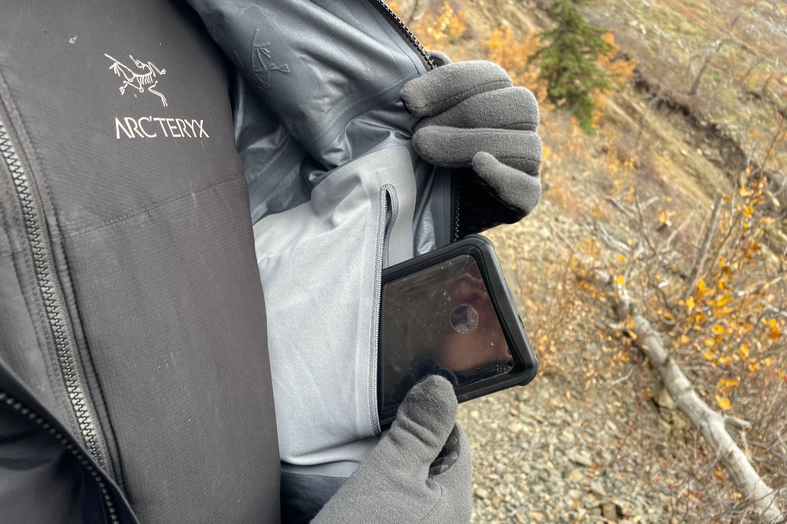 A closeup of a phone being put in an interior pocket of a black rain jacket.