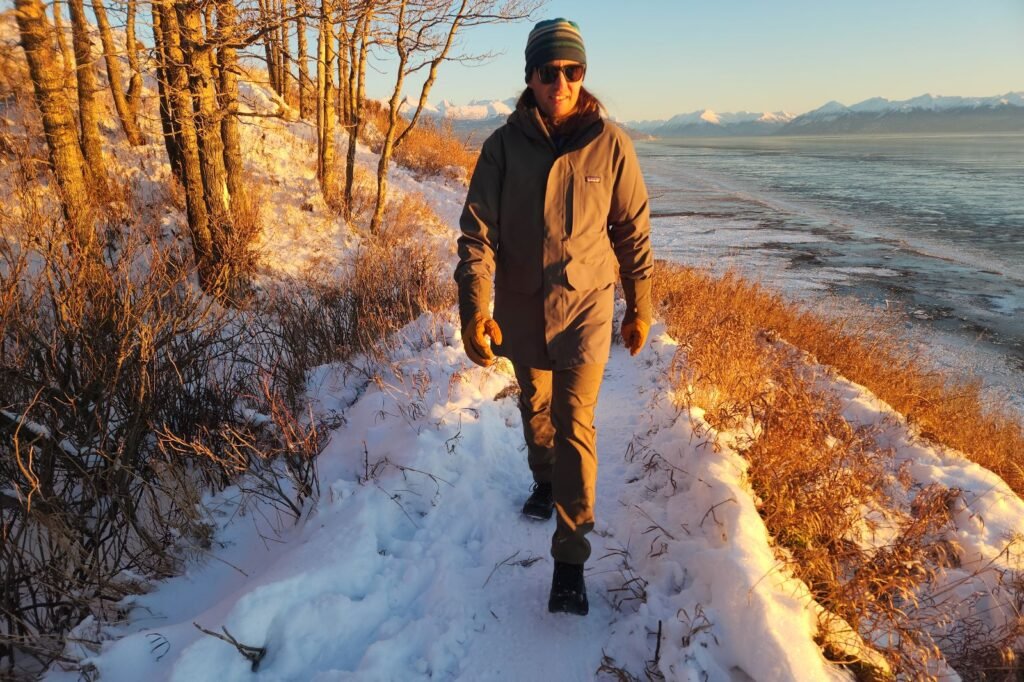 A man hikes along a snowy bluff above the ocean at sunset.
