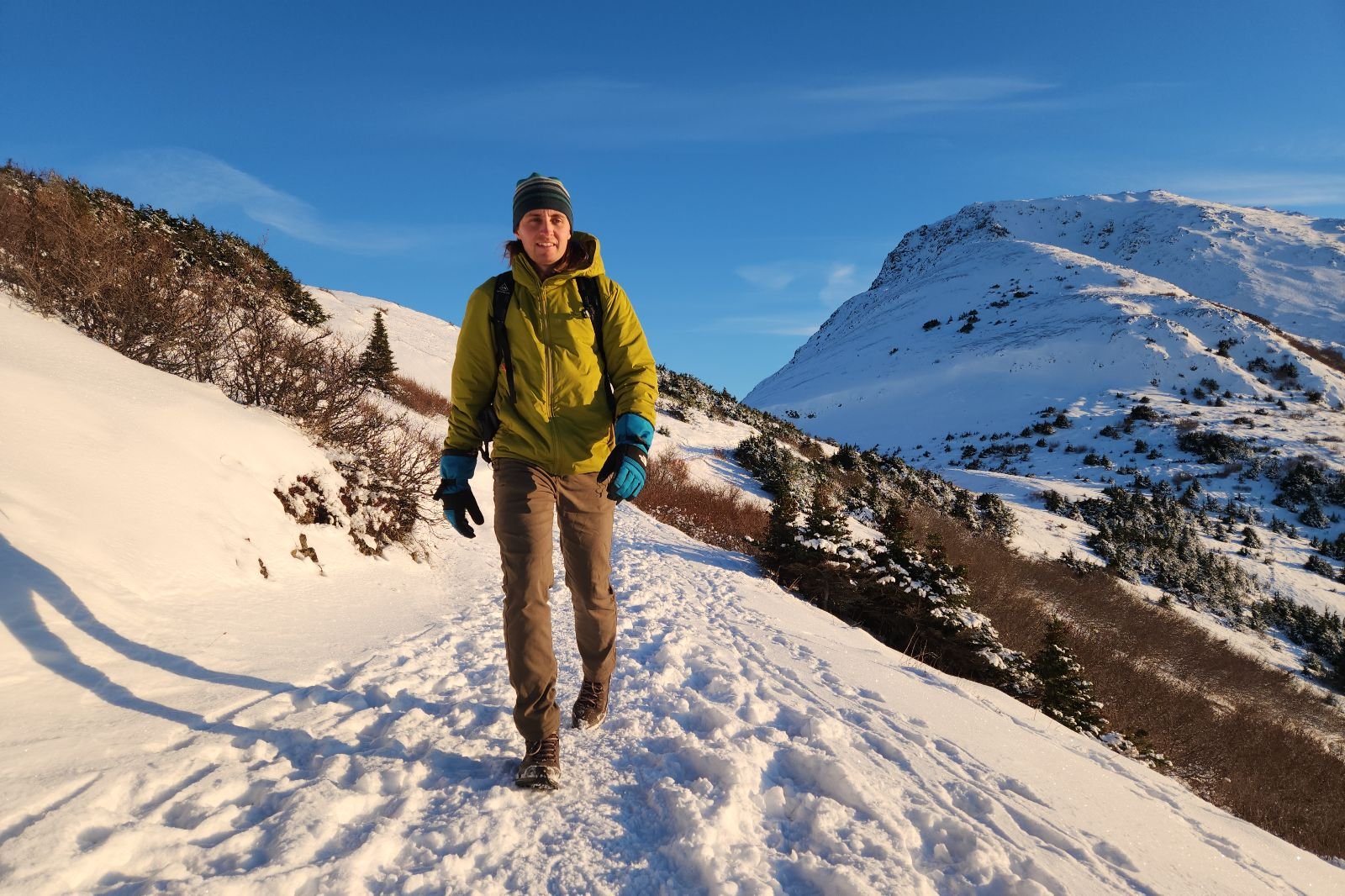 A man walks down a snowy trail with a mountain in the background.