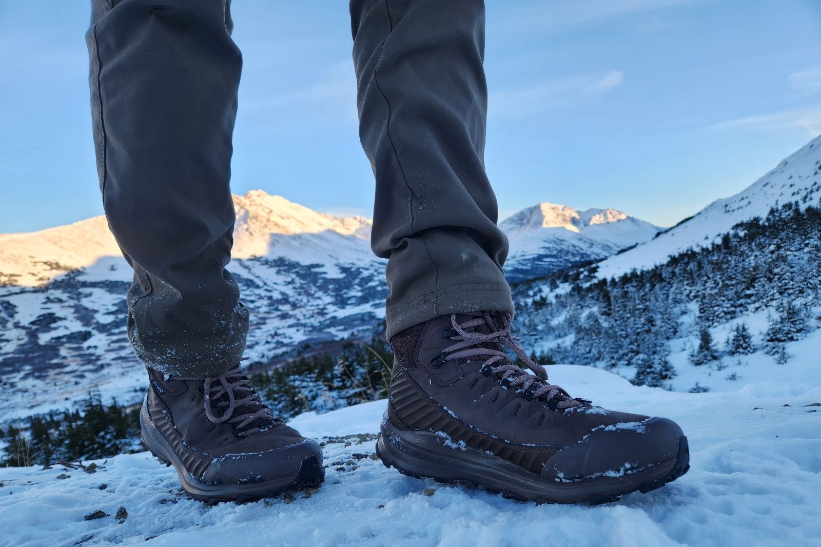 A pair of boots stands in front of a mountain view.