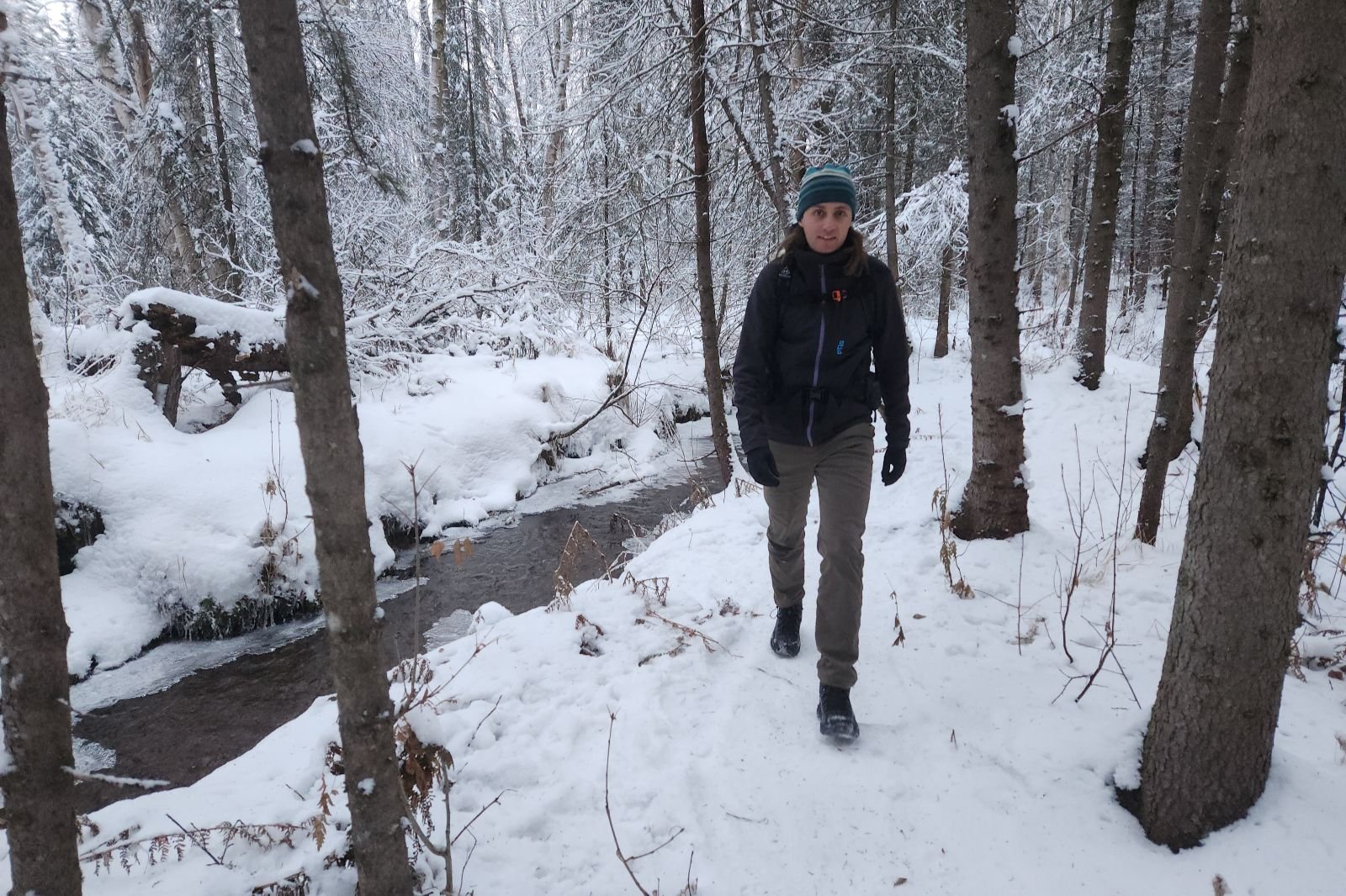A man walks along an ice covered creek.
