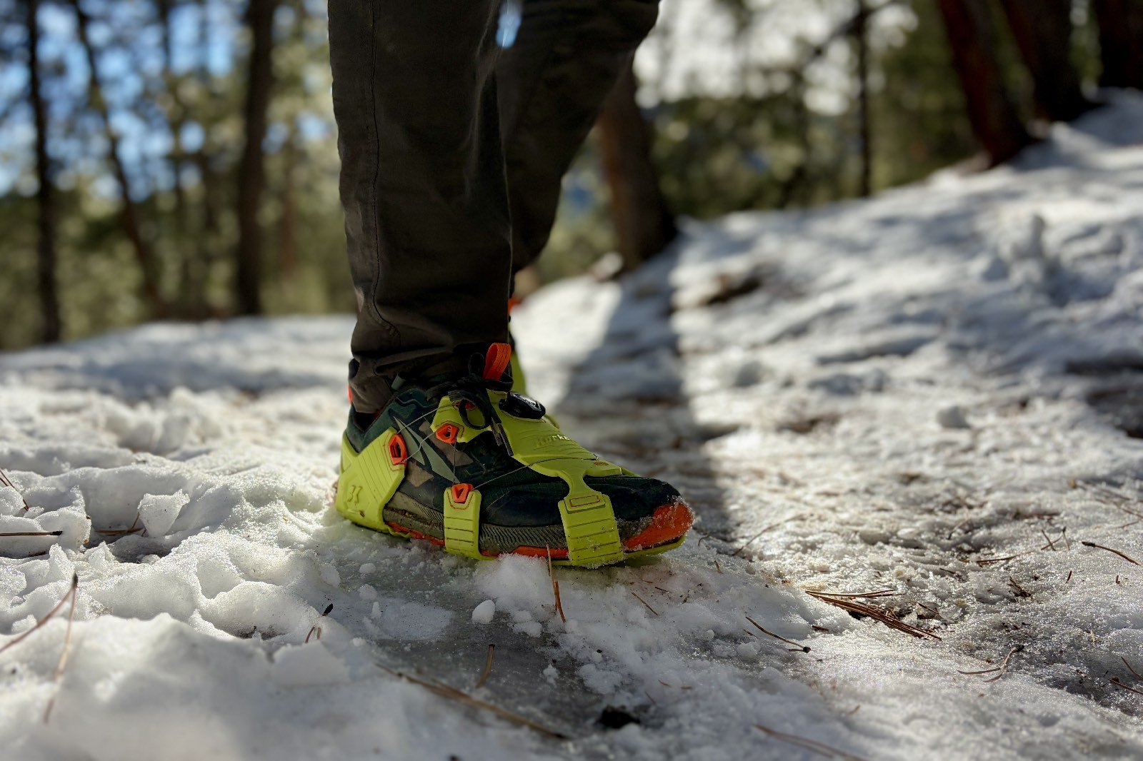 A close up of a hiker's shoe with traction device on a snowy trail