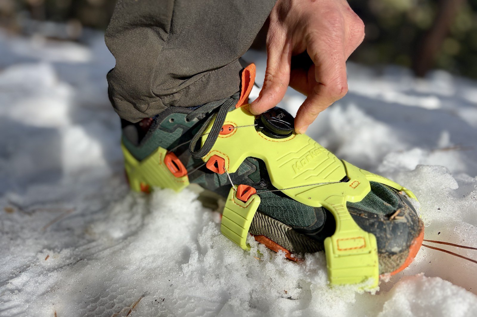 a close up of a hiker kneeling down to tighten the boa wheel on his ice cleats