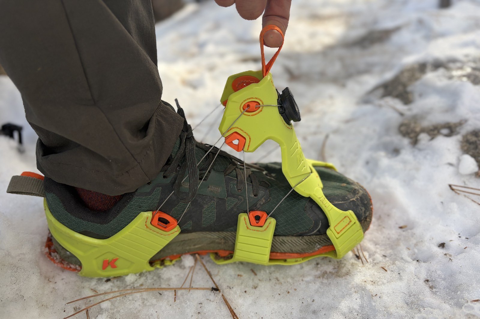 a close up of a hiker pulling the pull tab on his ice cleats, opening them up to their full capacity