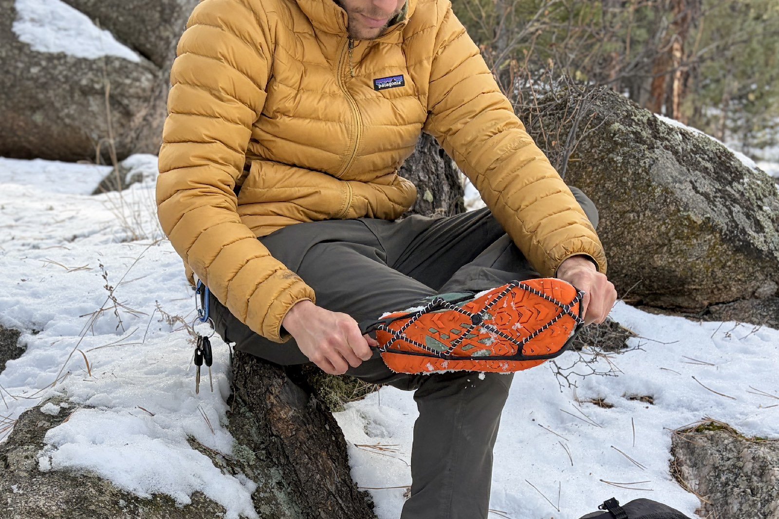 a hiker sits on a rock while stretching a yaktrax over his shoe