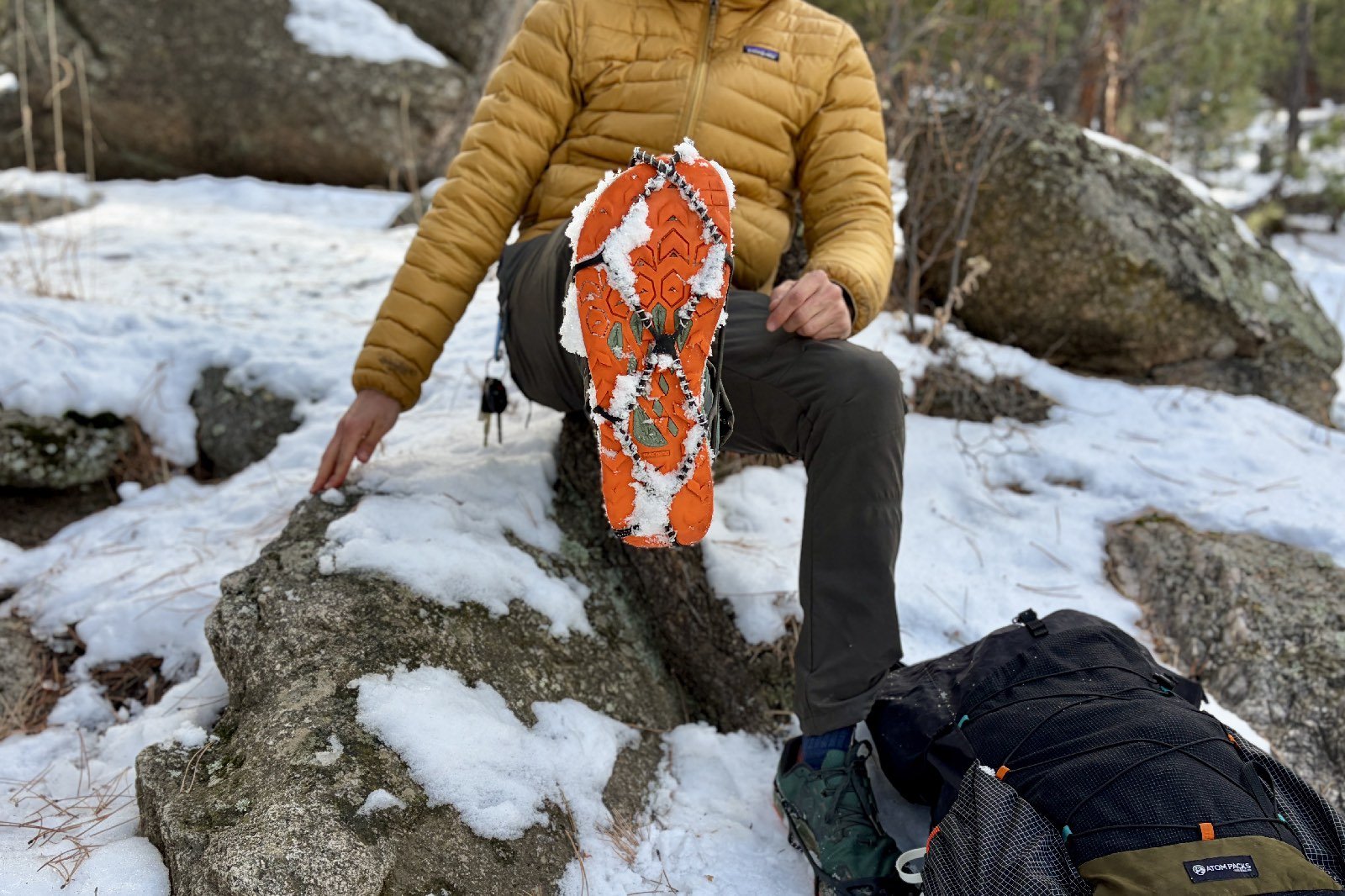 a hiker sits on a rock and shows his shoe with ice cleats attached to the camera