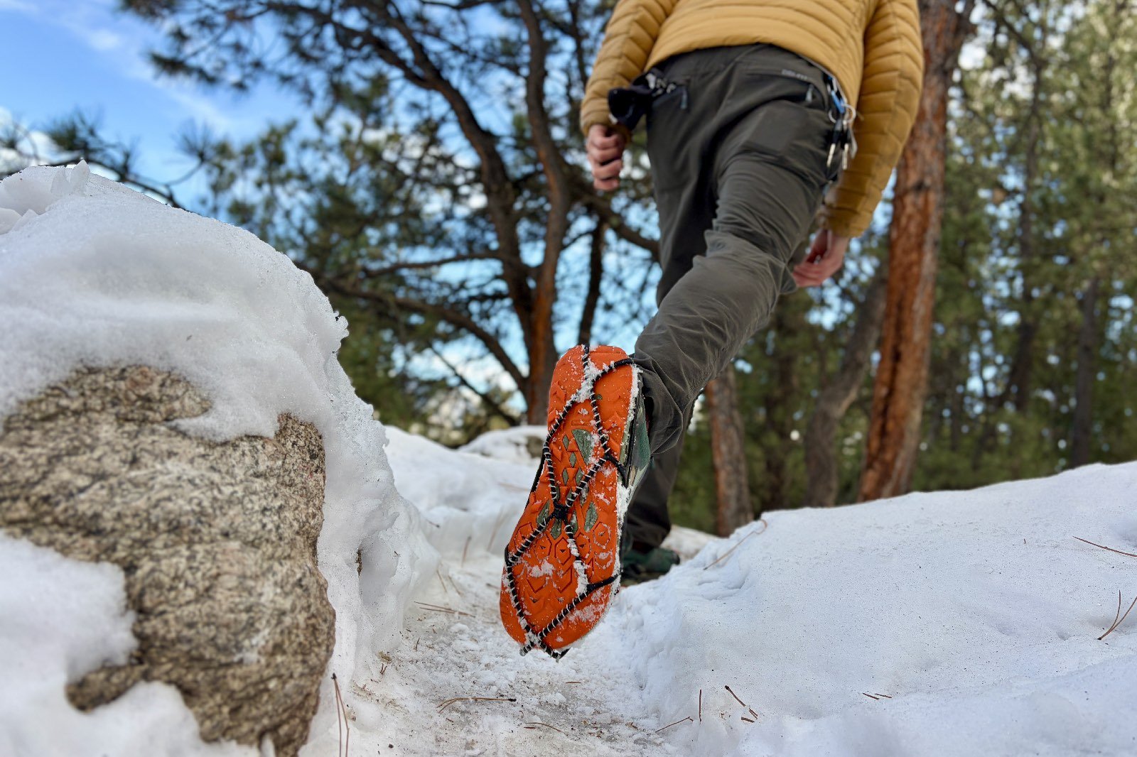 a hiker walks away from the camera showing the bottom of one shoe with a traction device attached