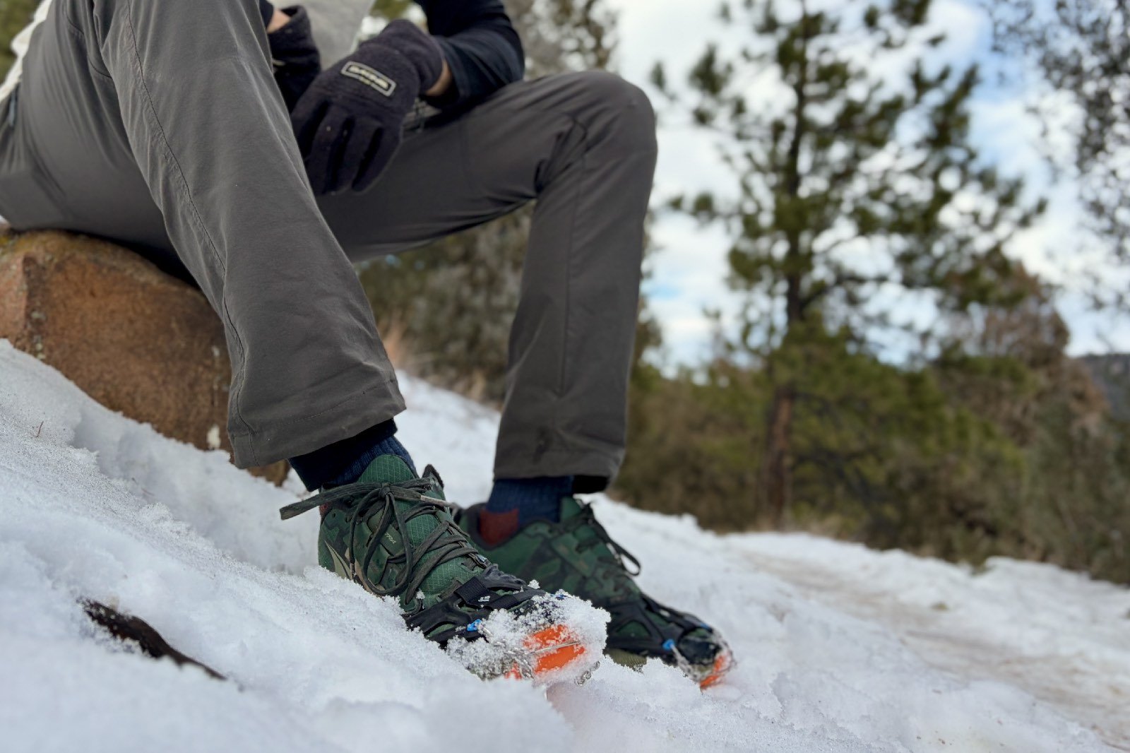 a hiker sits on a rock wearing a pair of ice cleats
