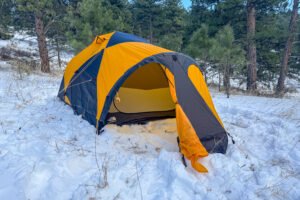 The North Face Mountain 25 with its vestibule door open, revealing the yellow inner tent and a snow-covered campsite around it.